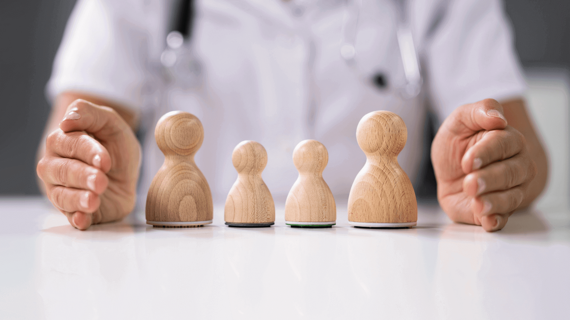 Vier Holzfiguren in unterschiedlichen Größen auf einem Tisch, gehalten von einer Person mit einem weißen Kittel.